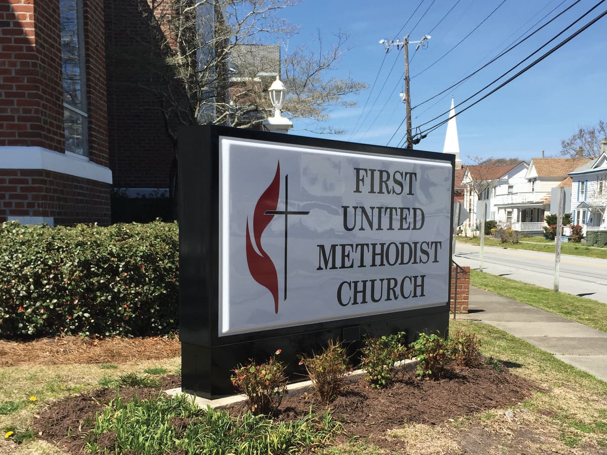 First United Methodist Church lit monument sign with flame-and-cross logo beside brick
