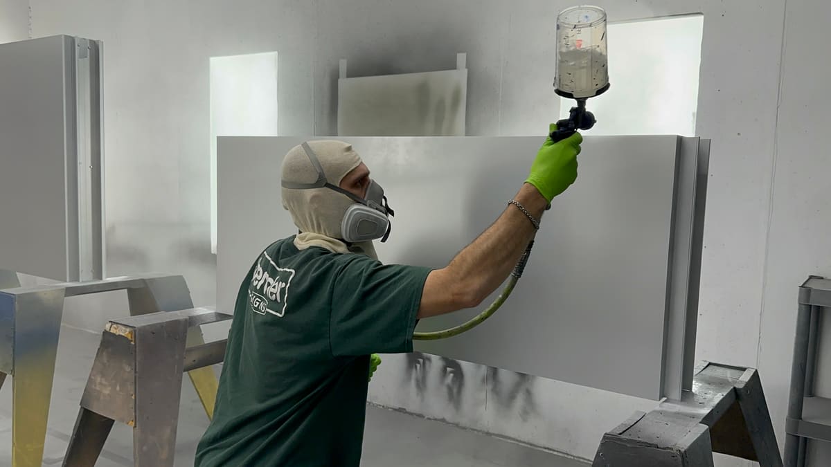 Painter in a respirator spraying a sign panel in the Bender paint booth